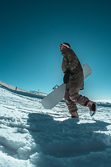 Image showing Snowboarder walking against blue sky