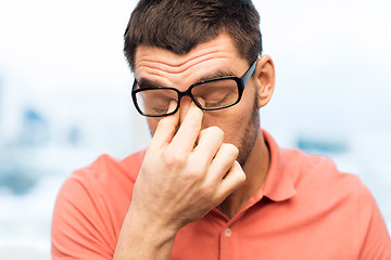 Image showing tired man in eyeglasses rubbing eyes at home