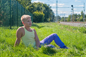 Image showing Young man in yellow sitting on the green grass