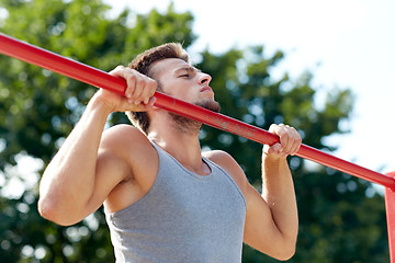 Image showing young man exercising on horizontal bar outdoors