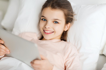 Image showing happy girl lying in bed with tablet pc at home