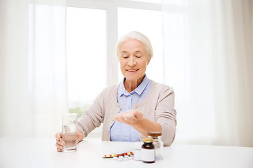 Image showing happy senior woman with water and medicine at home