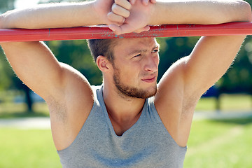 Image showing young man exercising on horizontal bar outdoors