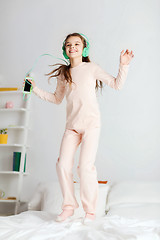 Image showing girl jumping on bed with smartphone and headphones