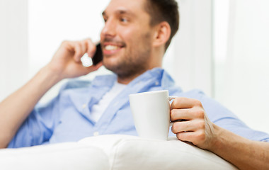Image showing smiling man with cup calling on smartphone at home