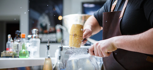 Image showing Bartender breaks ice with wooden hammer