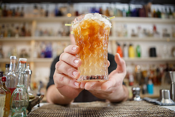 Image showing Bartender is standing in pub? holding cocktail and giving glass forward. Focus on beverage.