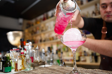 Image showing Close-up of bartender hand pouring pink cocktail drink in bar