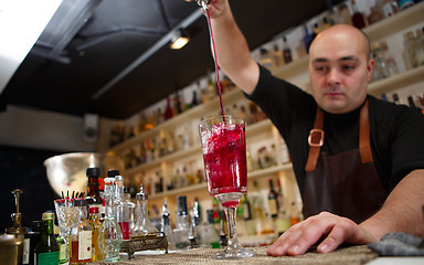 Image showing Bartender pouring red cocktail into glass at the bar