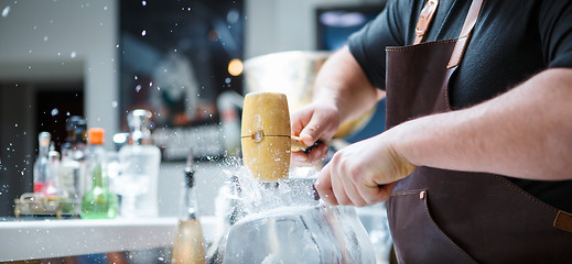 Image showing Bartender breaks ice with wooden hammer