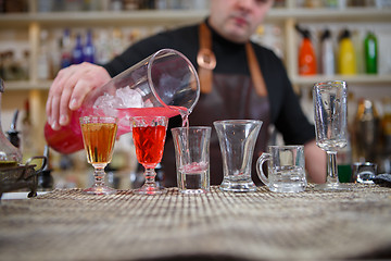 Image showing Bartender pours various of alcohol drink into small glasses on bar