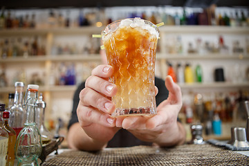 Image showing Bartender is standing in pub? holding cocktail and giving glass forward. Focus on beverage.