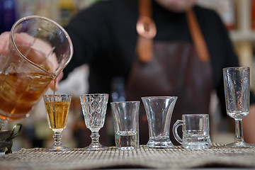 Image showing Bartender pours various of alcohol drink into small glasses on bar