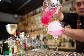 Image showing Close-up of bartender hand pouring pink cocktail drink in bar