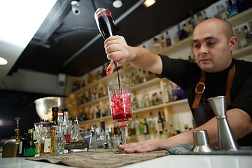 Image showing Bartender pouring red cocktail into glass at the bar