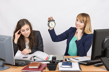 Image showing in the office, one employee is looking forward to the end of the day, while the other continues to work intensively