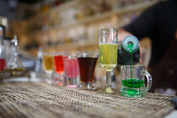 Image showing Bartender pours various of alcohol drink into small glasses on bar