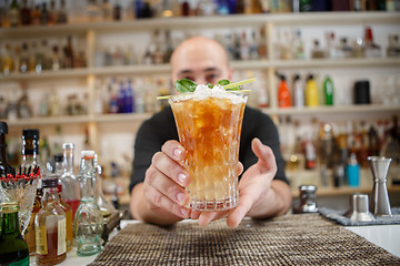 Image showing Bartender is standing in pub? holding cocktail and giving glass forward. Focus on beverage.