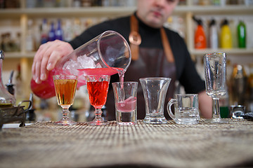 Image showing Bartender pours various of alcohol drink into small glasses on bar