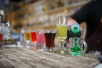 Image showing Bartender pours various of alcohol drink into small glasses on bar