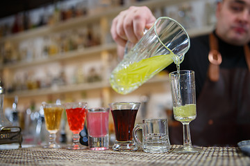 Image showing Bartender pours various of alcohol drink into small glasses on bar