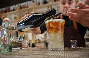 Image showing Bartender pouring cocktail into glass at the bar