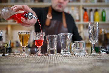 Image showing Bartender pours various of alcohol drink into small glasses on bar