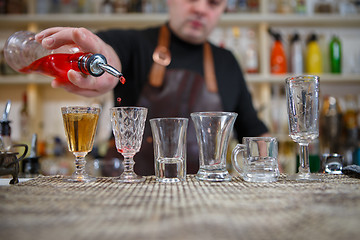 Image showing Bartender pours various of alcohol drink into small glasses on bar