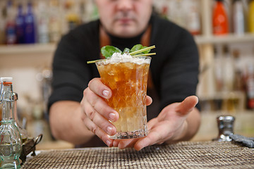 Image showing Bartender is standing in pub? holding cocktail and giving glass forward. Focus on beverage.