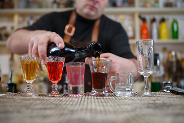 Image showing Bartender pours various of alcohol drink into small glasses on bar