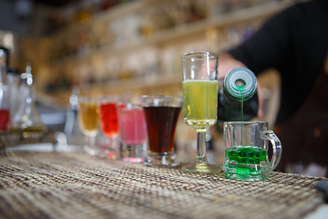 Image showing Bartender pours various of alcohol drink into small glasses on bar