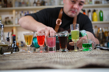 Image showing Bartender pours various of alcohol drink into small glasses on bar