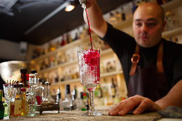 Image showing Bartender pouring red cocktail into glass at the bar