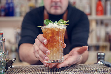 Image showing Bartender is standing in pub? holding cocktail and giving glass forward. Focus on beverage.