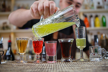 Image showing Bartender pours various of alcohol drink into small glasses on bar