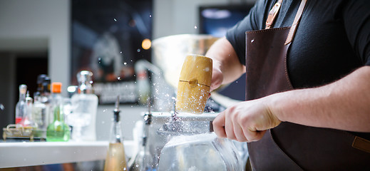 Image showing Bartender breaks ice with wooden hammer