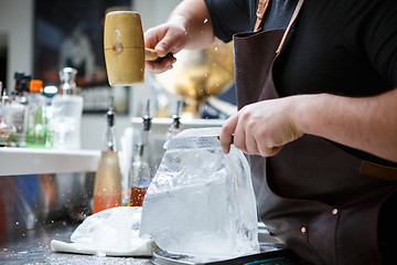 Image showing Bartender mannually crushed ice with wooden hammer and metal knife.