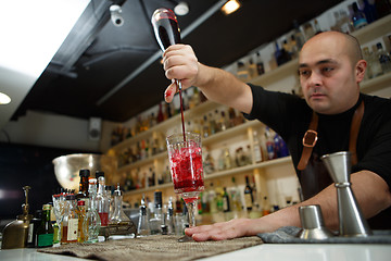 Image showing Bartender pouring red cocktail into glass at the bar