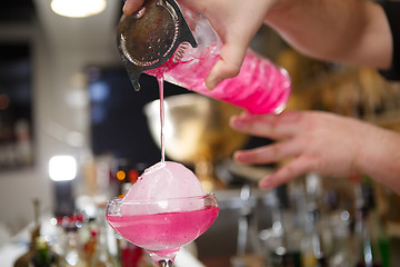 Image showing Close-up of bartender hand pouring pink cocktail drink in bar