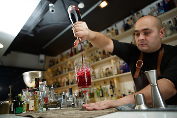 Image showing Bartender pouring red cocktail into glass at the bar