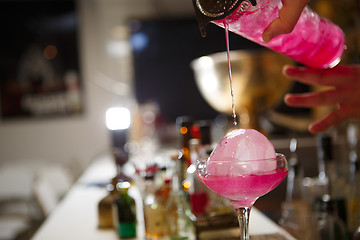 Image showing Close-up of bartender hand pouring pink cocktail drink in bar