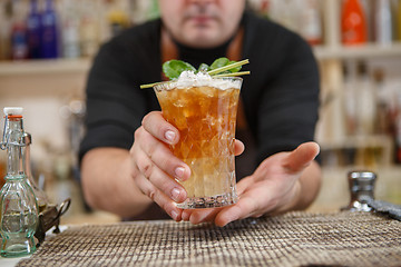 Image showing Bartender is standing in pub? holding cocktail and giving glass forward. Focus on beverage.