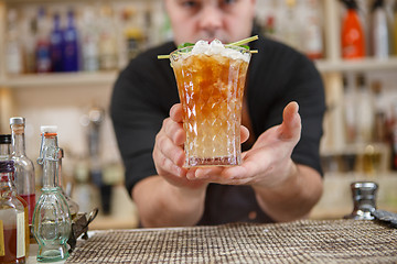 Image showing Bartender is standing in pub? holding cocktail and giving glass forward. Focus on beverage.