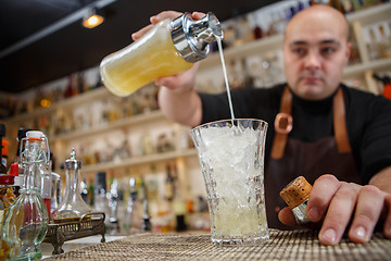 Image showing Bartender pouring cocktail into glass at the bar