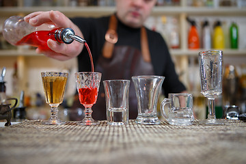 Image showing Bartender pours various of alcohol drink into small glasses on bar