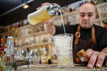 Image showing Bartender pouring cocktail into glass at the bar