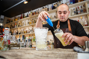 Image showing barman using a hand mixer to prepare drink in  bar or pub