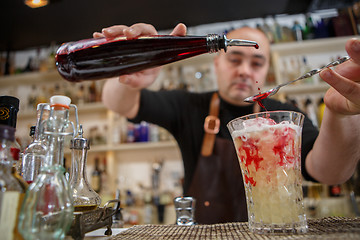 Image showing Bartender pouring cocktail into glass at the bar