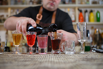 Image showing Bartender pours various of alcohol drink into small glasses on bar