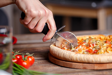 Image showing Slicing fresh pizza with roller knife. 